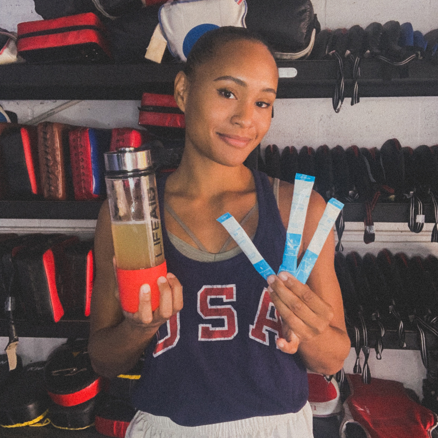 A woman holding three Focusaid GO sachets and a LIFEAID water bottle.