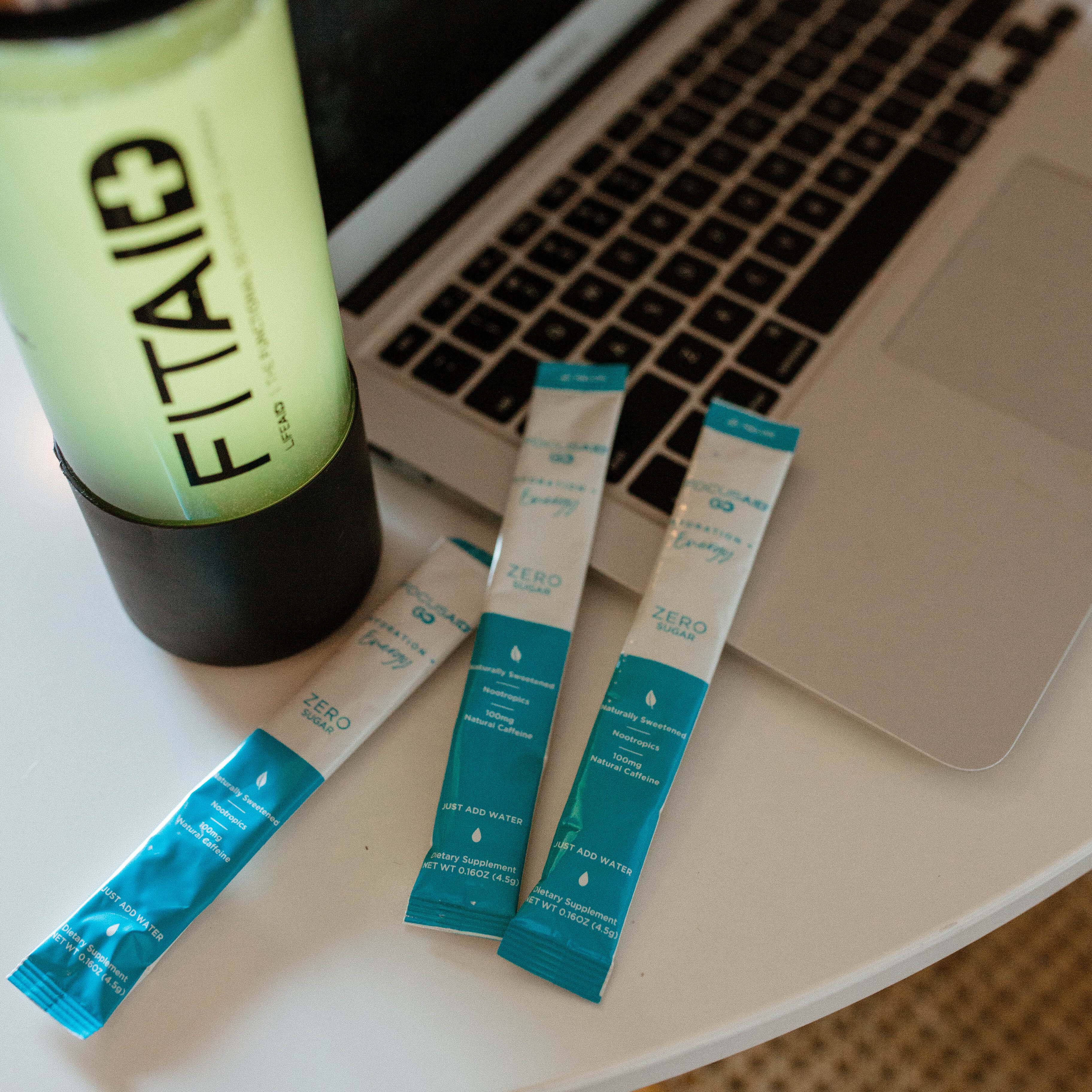Three Focusaid GO sachets next to a FITAID water bottle, and a laptop.
