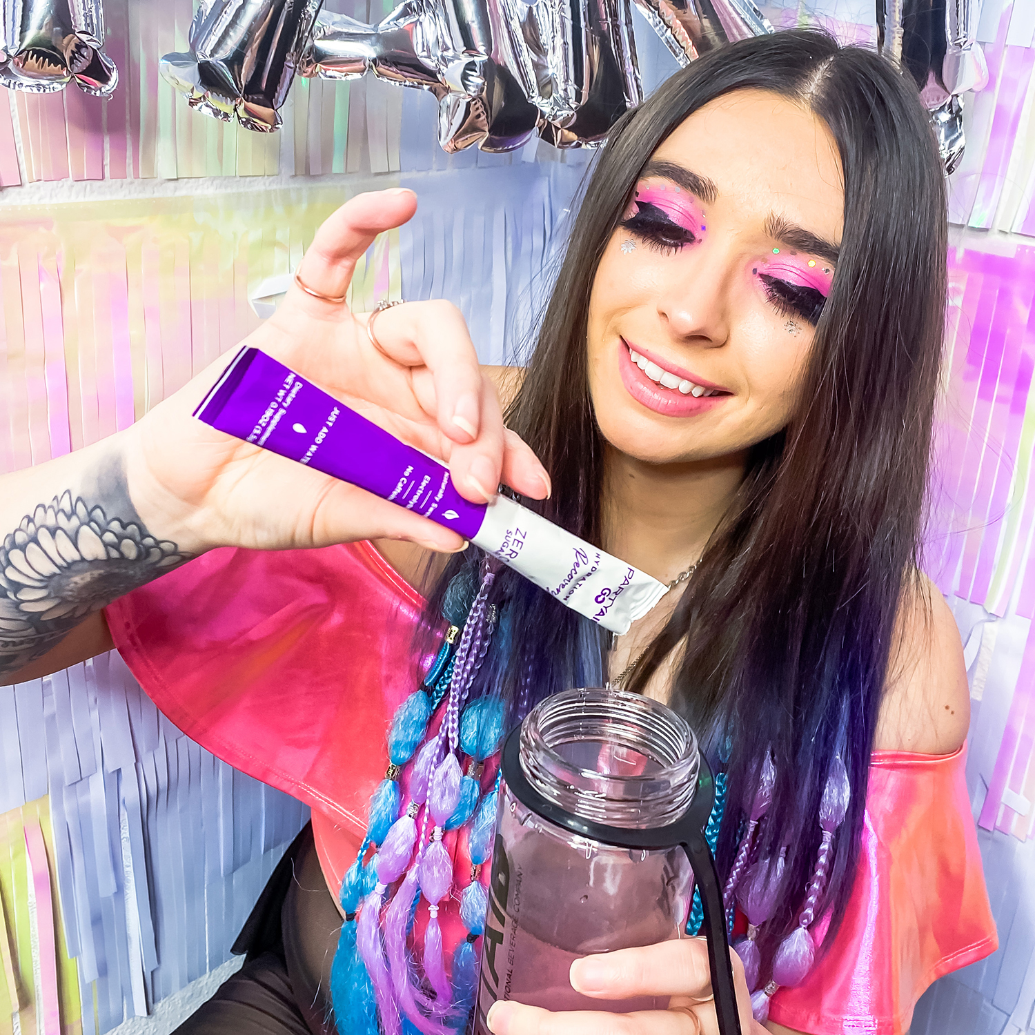 A woman holding a Partyaid GO sachet while pouring it's content to a water bottle.