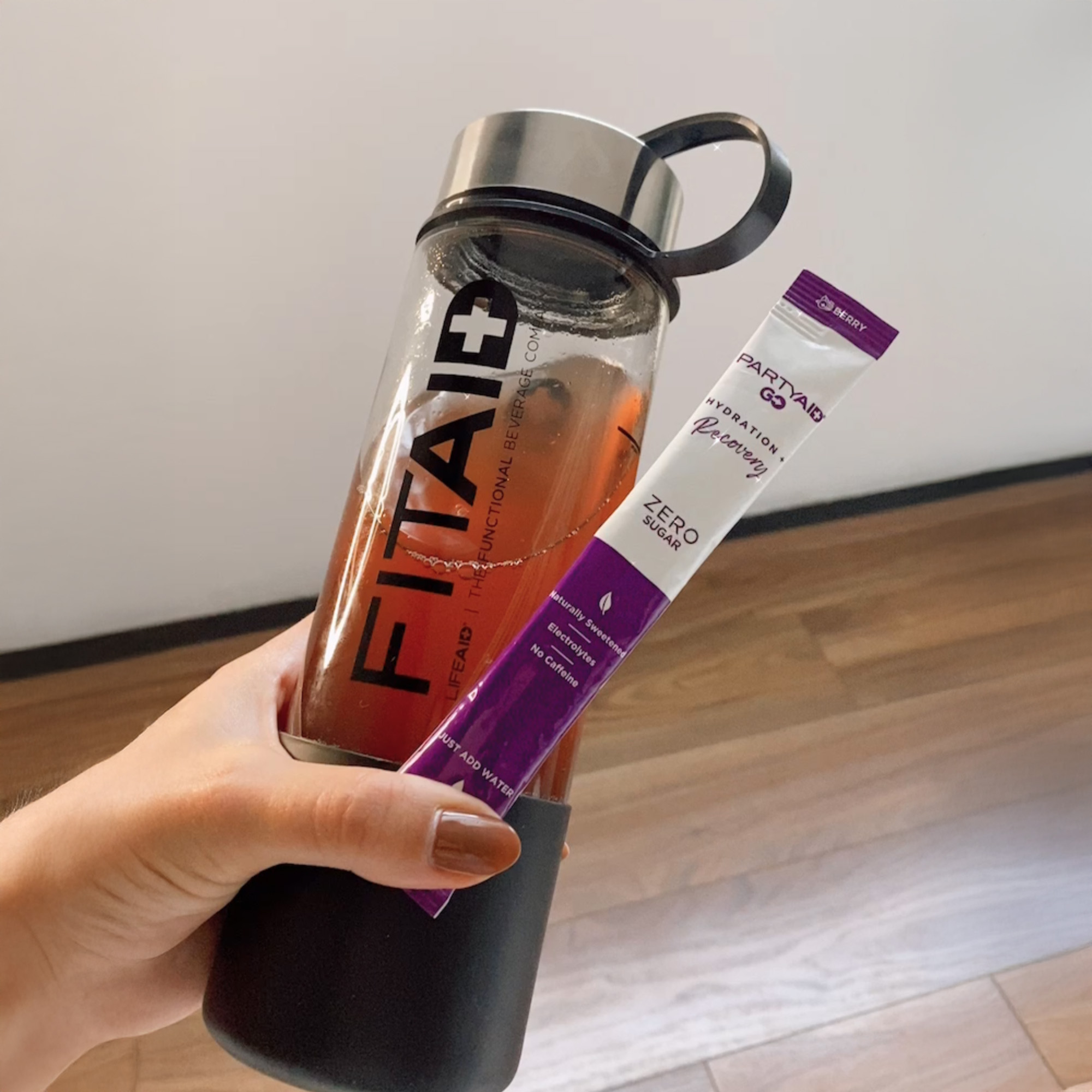 A person holding a sachet of Partyaid GO and a FITAID water bottle.