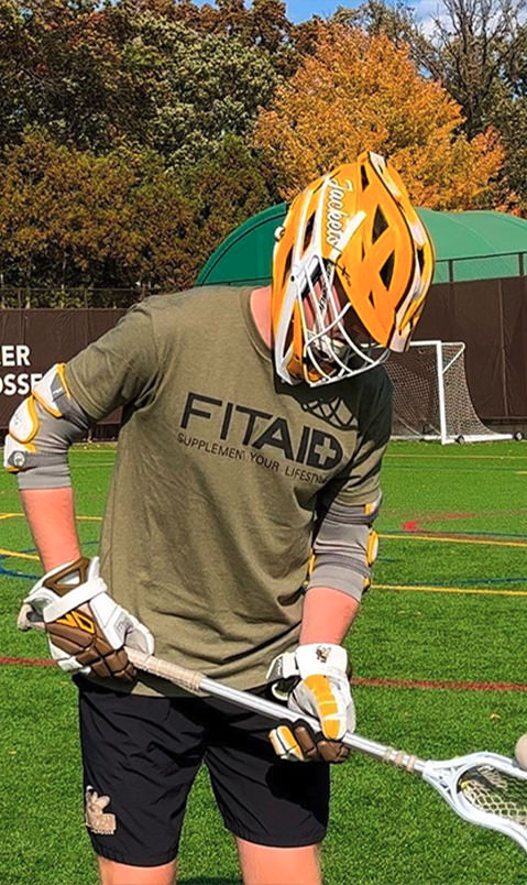 Brand ambassador wearing yellow and white lacrosse gear and an army green FITAID shirt with black text