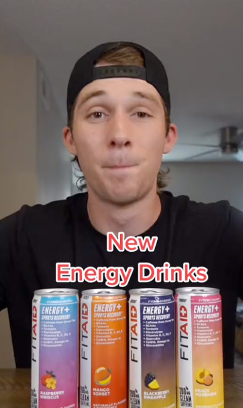 Brand ambassador in a black shirt and black hat with four FITAID Energy drinks in front. 