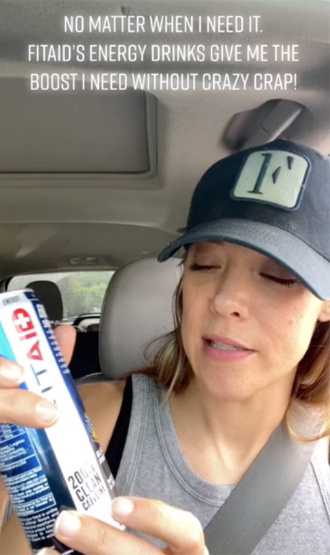 Brand ambassador in the car wearing a black hat, holding a FITAID can, with text that reads across the top of the image saying, "NO MATTER WHEN I NEED IT. FITAID'S ENERGY DRINKS GIVE ME THE BOOST I NEED WITHOUT CRAZY CRAP!"