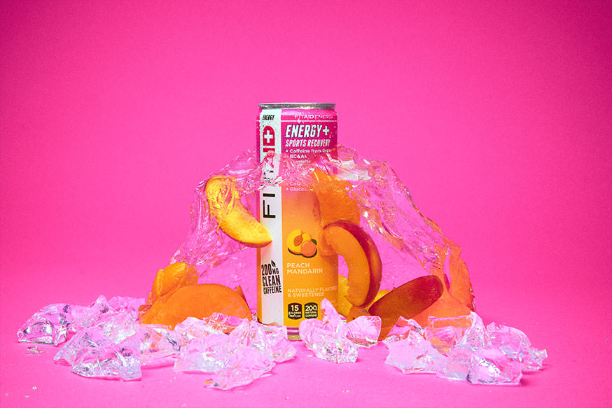 A can of FITAID Energy Peach Mandarin surrounded by peach and ice cubes.
