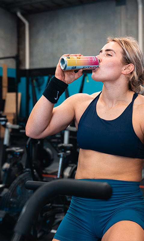 Brand ambassador in the gym, wearing a navy blue sports bra and shorts, drinking a can of FITAID